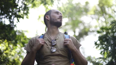 young traveller backpacker taking big breath inhaling fresh clean air in green natural park with sunny blurred background