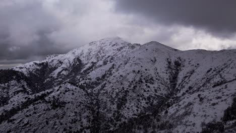 Aerial-of-snowy-white-mountain-peak-with-dramatic-cloudy-sky,-forward,-day