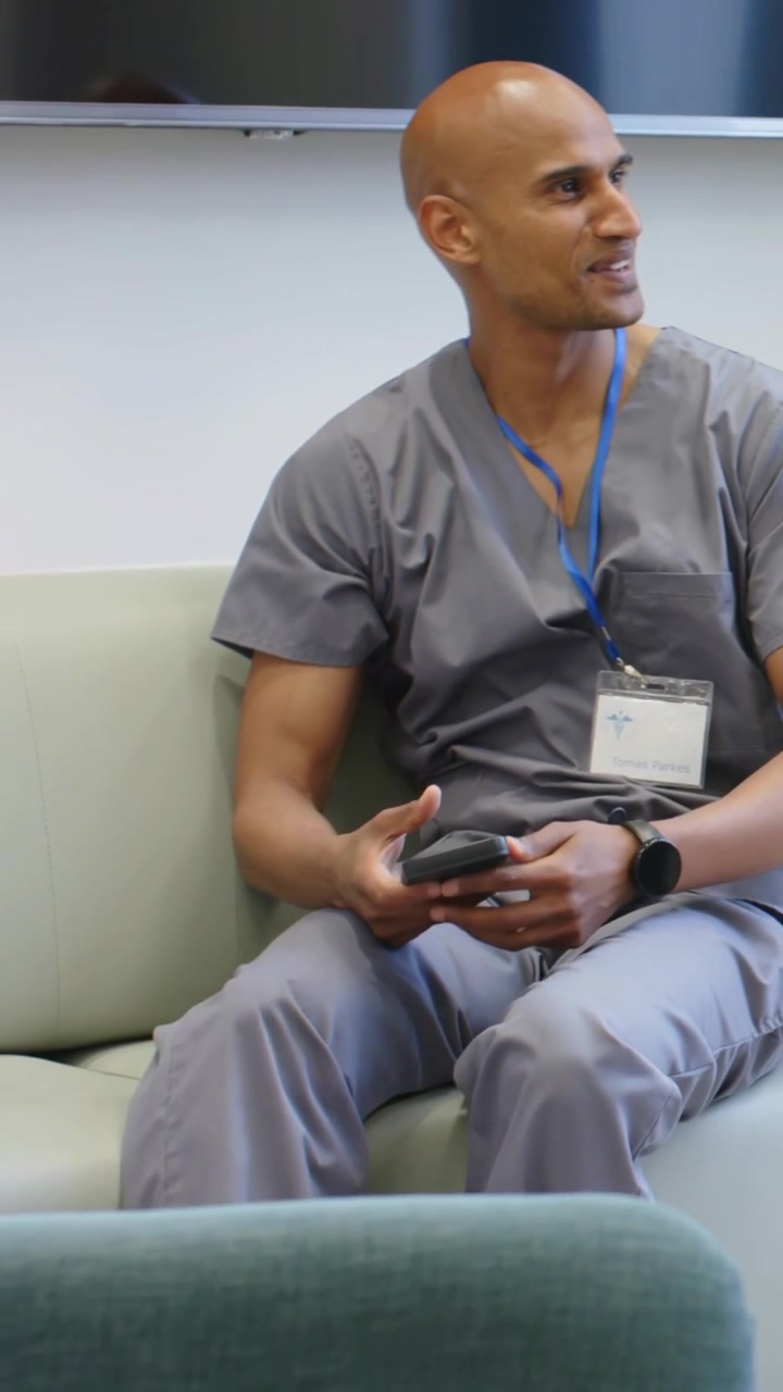 Video verticale: Uomo in camice medico che si siede in salotto, risponde a una chiamata, tiene in mano il telefono e parla.