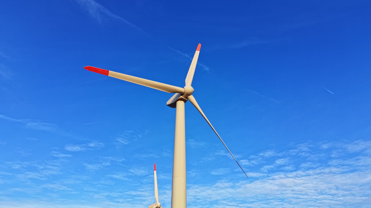 Turbine eoliche si ergono alte contro un cielo blu brillante con poche nuvole in un sito di energia rinnovabile durante il giorno in una zona rurale