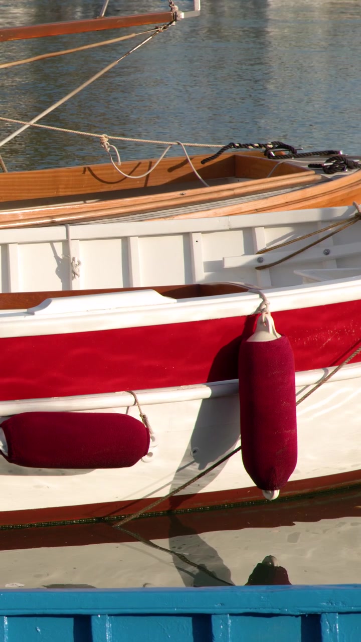 Primo piano statico dello scafo di un classico yacht in legno con parabordi rossi che galleggiano in acqua calma.