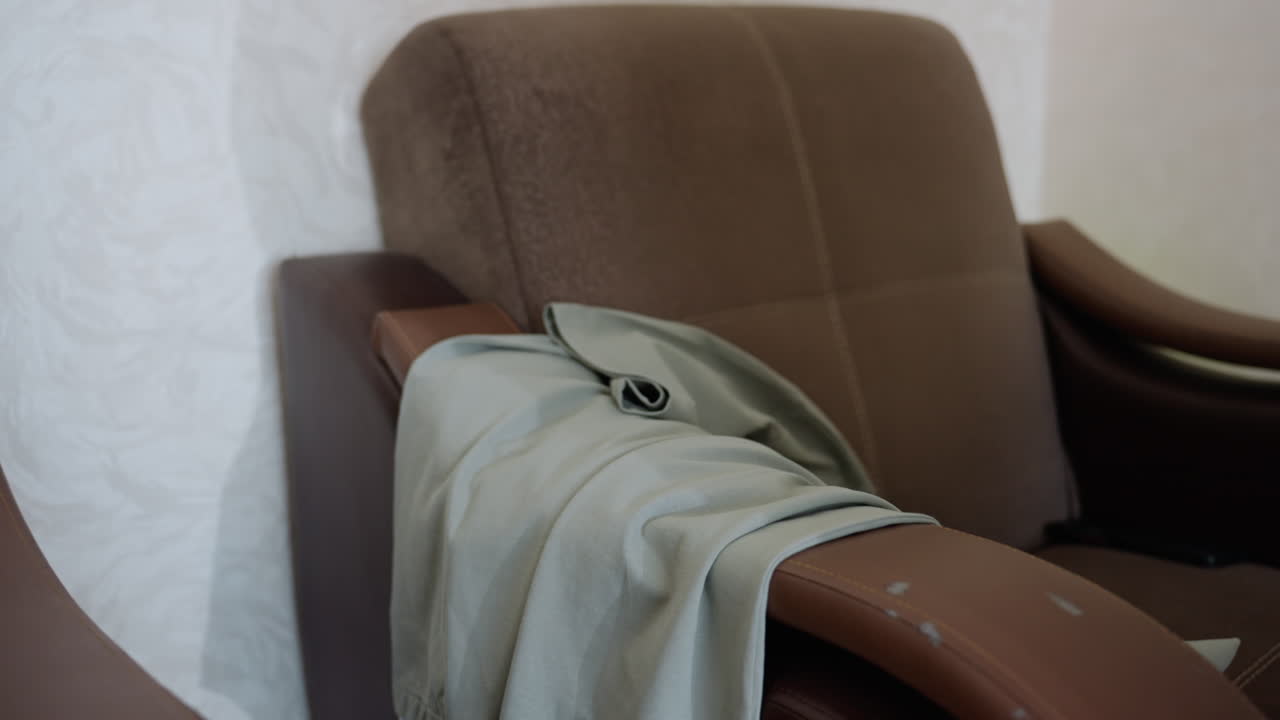Close up rear view of kid in black singlet placing trouser on couch armrest then arranging top over it as part of daily routine tidying home space showing gesture of responsibility