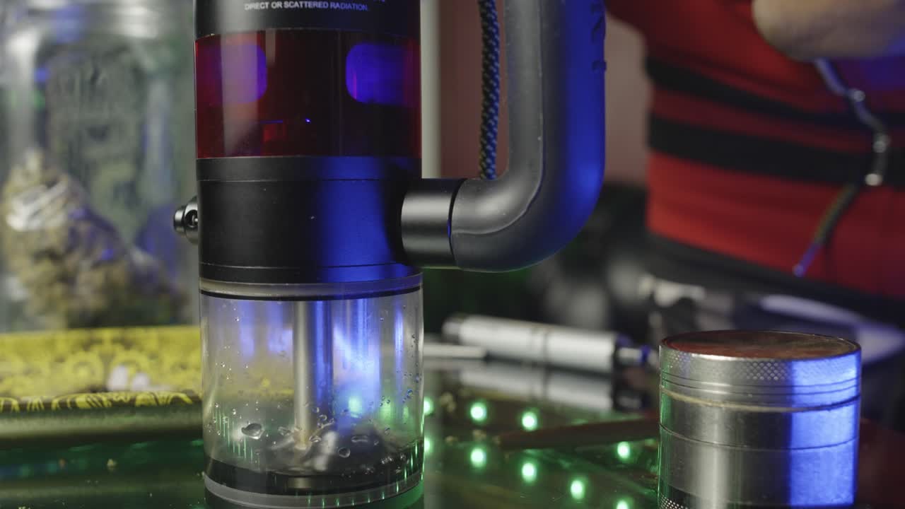 cerca de la cámara de un bong de agua electrónico mientras burbujea y se llena de humo mientras alguien golpea la pipa de hierba y luego exhala el humo de la marihuana