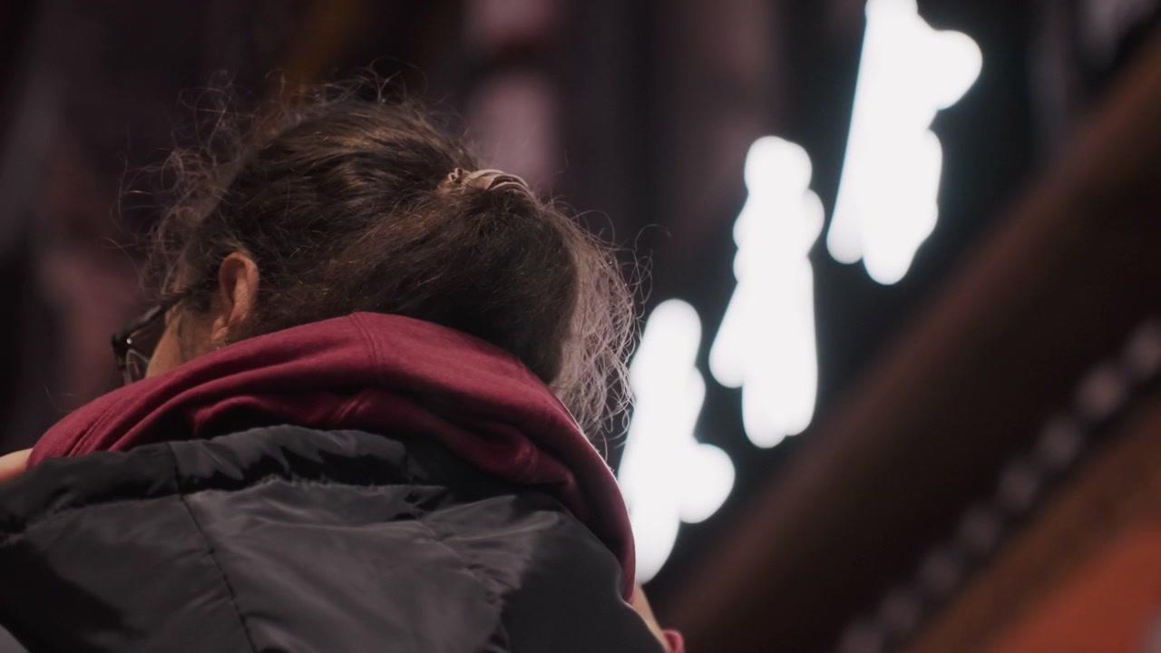 Passeggiata notturna in città. Una silhouette misteriosa si ferma sotto la vibrante illuminazione al neon della città. Una persona enigmatica con il cappuccio osserva le insegne luminose in un vivace ambiente urbano notturno.