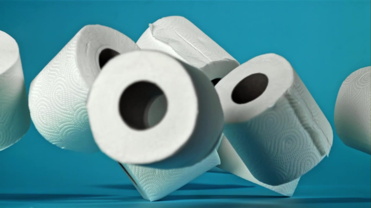 Weiße Toilettenpapierrollen fallen in Zeitlupe auf blauem Hintergrund