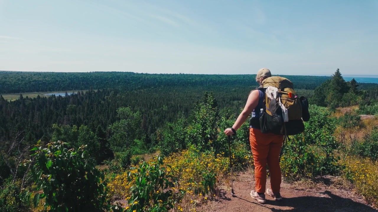 A backpacker walking up to the edge of a cliff for a massive forest landscape view of miles of wilderness.