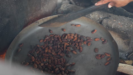 close up of one hand mixing the cocoa beans inside a pan