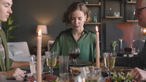 mujer adulta sosteniendo las manos de sus parientes y rezando antes de la comida mientras se sienta en la mesa de la cena en casa