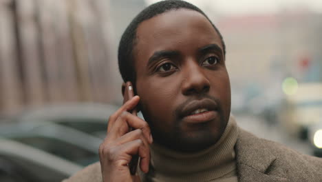 Close-up-view-of-African-American-businessman-wearing-coat-talking-on-the-phone-seriously-in-the-street-in-autumn