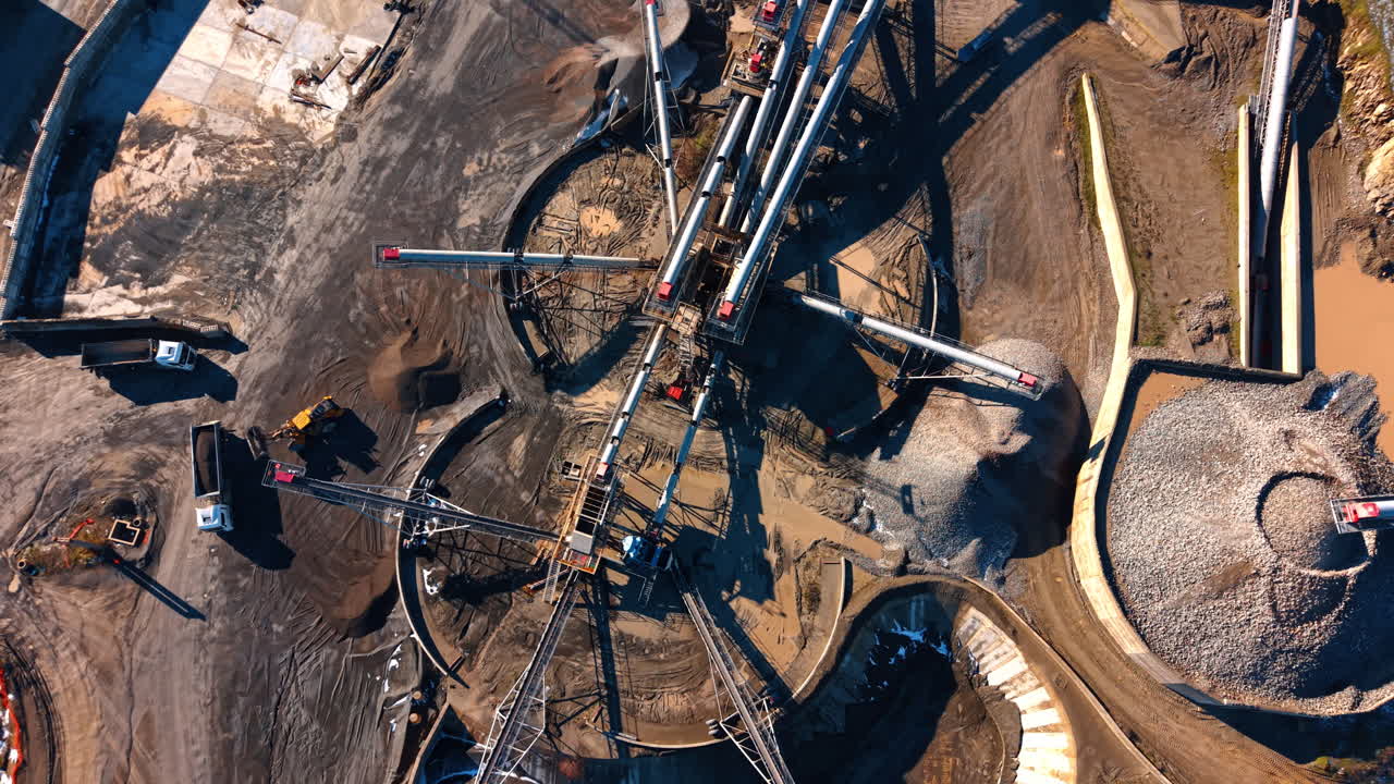Industrial quarry site with machinery and conveyor network. Overhead view of a granite processing plant featuring conveyors, trucks, and loaders at work