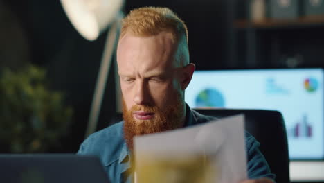 un hipster barbudo analizando datos en su computadora portátil y documentos en la oficina.