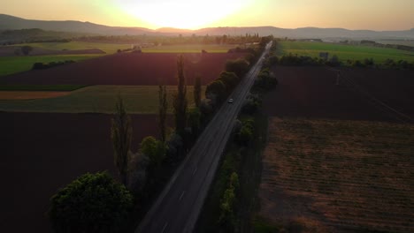aerial of cars dribing on a road countryside nect to fields at summer sunset