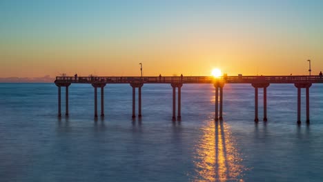 Time-lapse-during-sunset-of-beautiful-california-pier-and-smooth-ocean-waves-with-people-walking-around