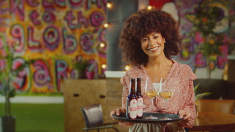 Portrait-Of-Smiling-Female-Server-Holding-Tray-Of-Drinks-In-Cool-Bar-Or-Club