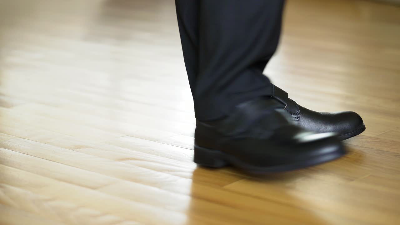 Man's legs with suit trousers and black leather shoes walking on the wooden floor. Young male walks on a spot and shows his new shoes.Close-up