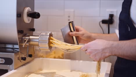 Nahaufnahme-Der-Hände-Des-Küchenchefs,-Die-Hausgemachte-Spaghetti-Aus-Der-Maschine-Schneiden