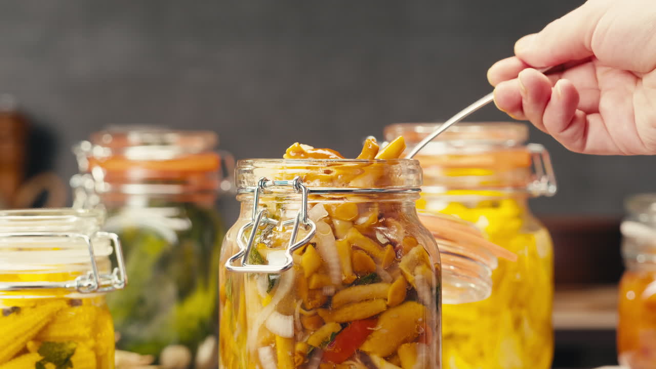 Fermented food in glass cans on table close-up. Preservation of vegetables in glass jars. Fermentation preserved mini corns, kimchi, cucumbers, mushrooms with spices.