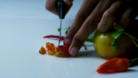 movimiento lento de las manos cortando pimienta roja de bombay con variedad de verduras frescas en el lado