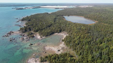 Aerial-view-of-rocky-forested-lake-shoreline-bay-and-small-inland-lake,-Lake-Huron,-Michigan