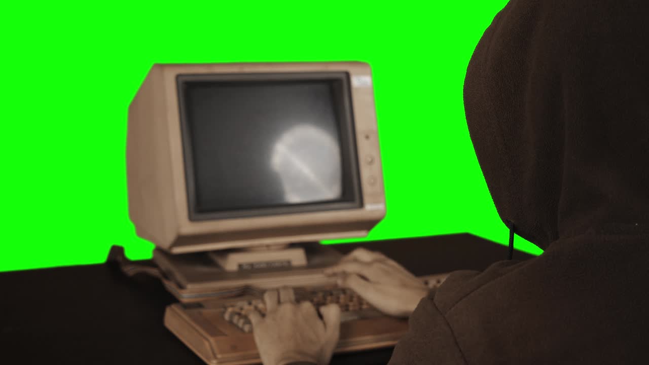 Rear view of hooded man using an old computer
