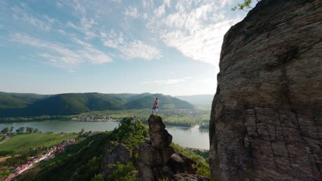 Tipo-Legendario-En-La-Cima-De-La-Montaña,-Drone-Rápido-Fpv,-Toma-Aérea-Con-Velocidad,-Pose-Del-Rey-Del-Mundo,-Alpinista,-Persona-En-La-Cima-De-La-Colina,-Descripción-General-Del-Paisaje-Del-Valle-Del-Río-Danubio,-Volando-Alrededor