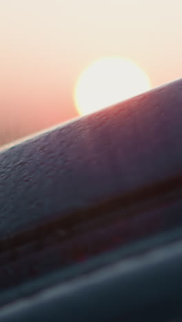 car stands under rains sprays dusk sun closeup. black auto with small water drops at rainstorm in evening countryside. travelling on rainy season