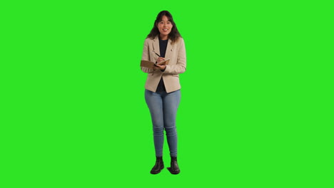 Full-Length-Studio-Portrait-Of-Female-Teacher-With-Notebook-Taking-Class-Register-Standing-Against-Green-Screen