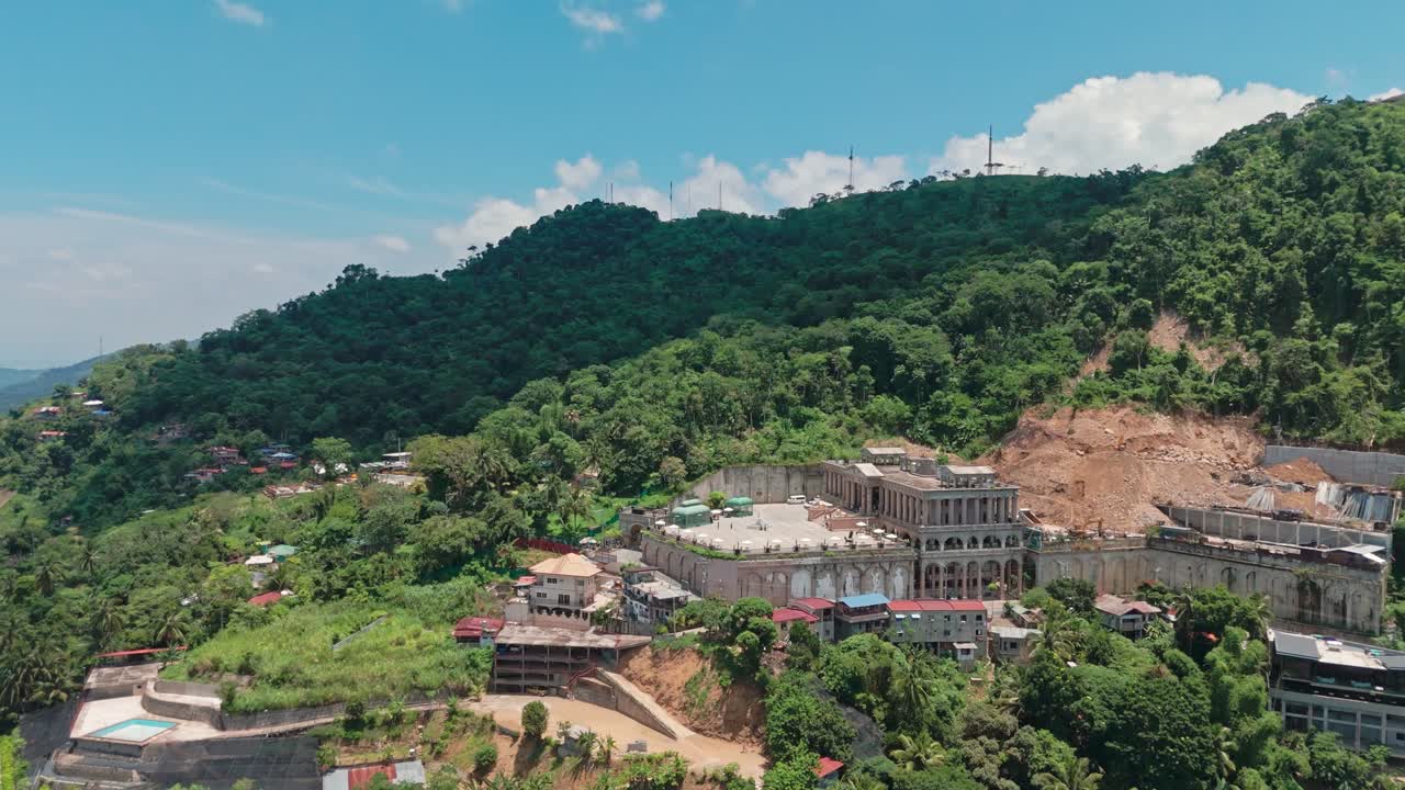 Aerial view of a neoclassical estate under construction on a lush tropical hillside in the Philippines. Surrounded by dense jungle and rural mountain communities