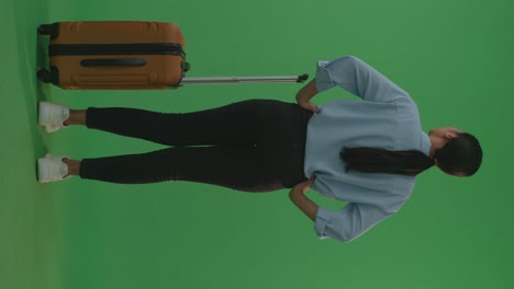 full body of back view asian woman traveler with luggage standing with arms akimbo in the green screen background studio, during sunset time