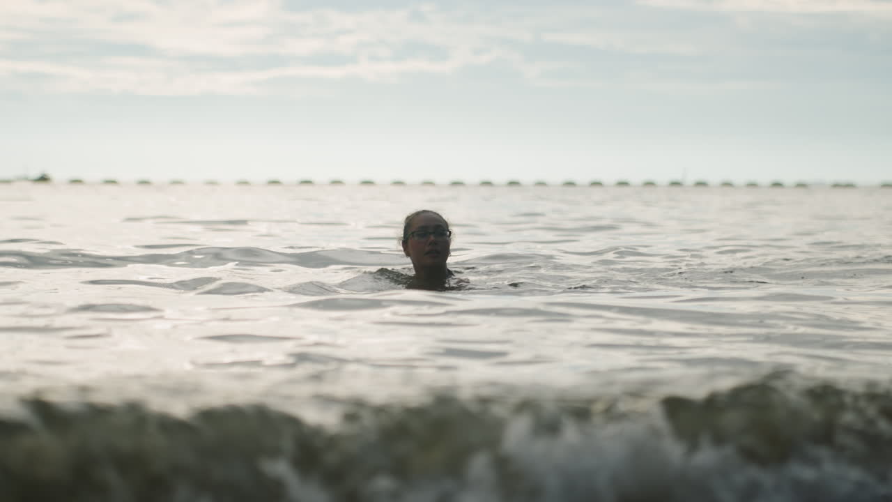Swimmer rising through choppy sea surf head breaks foam and spray, waves crashing foreground, camera close, dramatic light, lifeguard drill and endurance training, survival practice, determined ascent