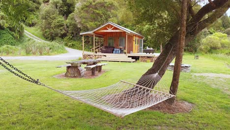 a hammock between trees in front of a wood cabin in nature in new zealand