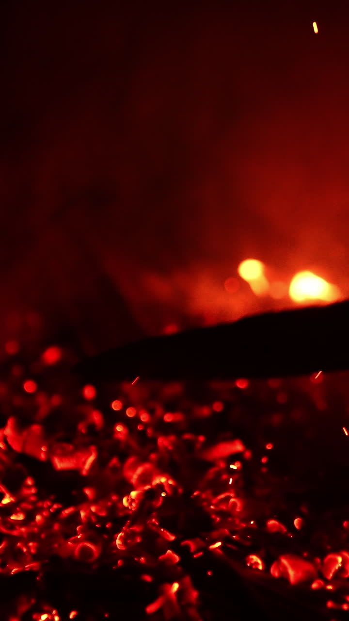 Unknown person moving the fire burning out. Smoldering embers sparkling beautifully. Black backdrop. Vertical video
