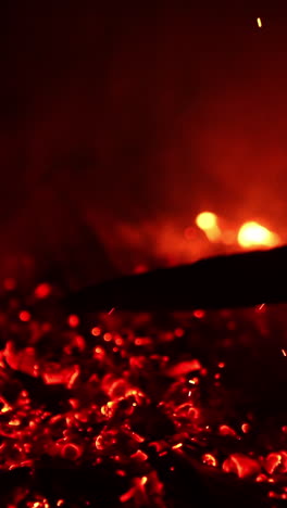 unknown person moving the fire burning out. smoldering embers sparkling beautifully. black backdrop. vertical video
