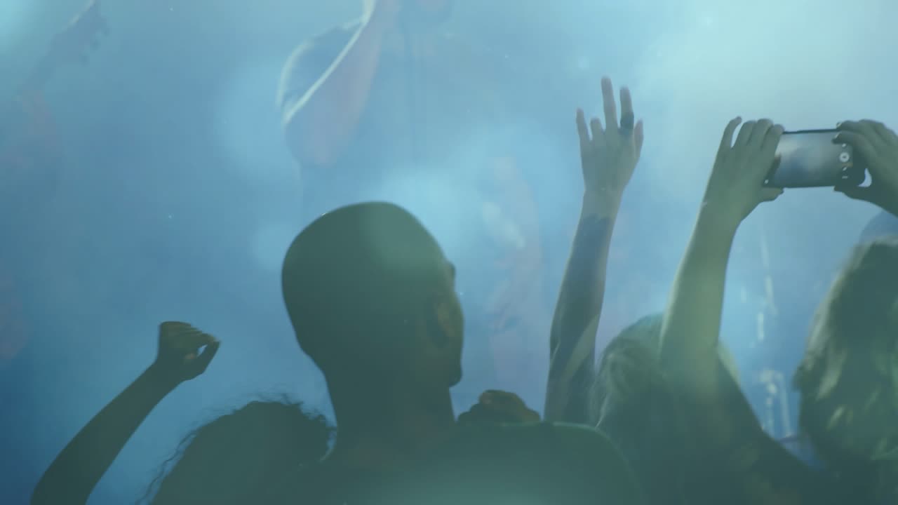 Audience raising phones to record and waving as singer starting music set, light bokeh hiding stage