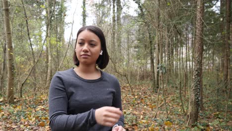young woman puts on her earphones on a leaves covered forest road in autumn - tracking shot