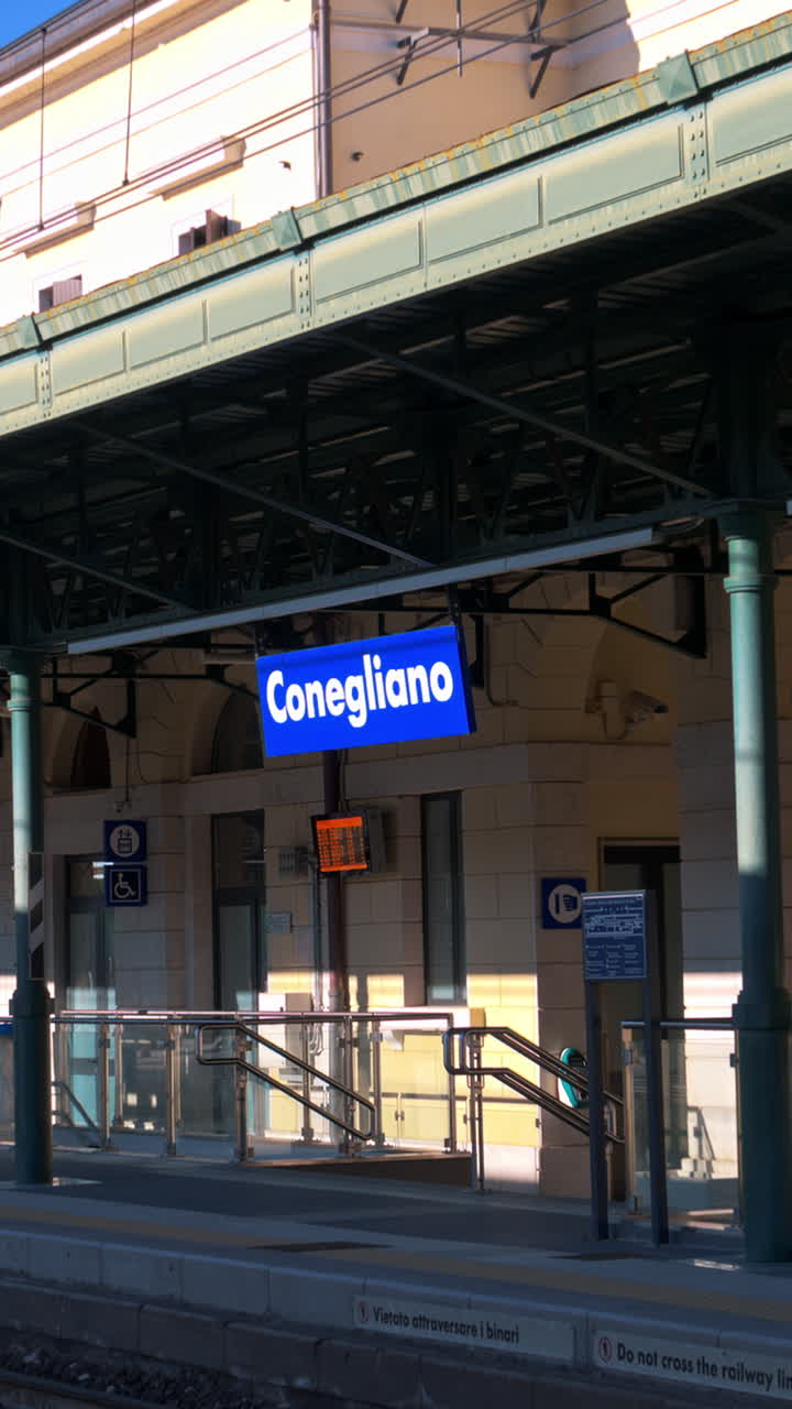 People waiting at the Conegliano train station on a sunny day. Vertical, Conegliano, Italy