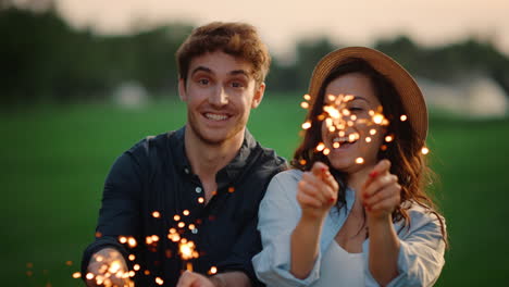 una pareja feliz jugando con luces bengalíes en el prado.