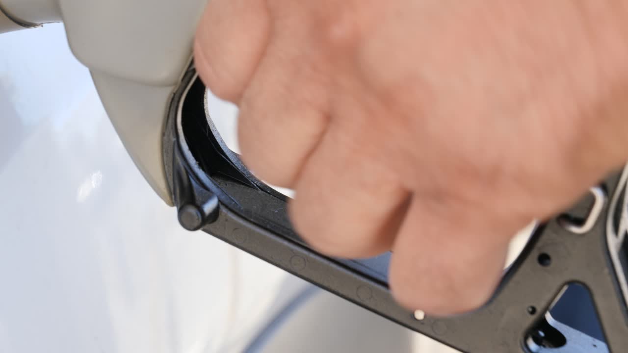 primer plano de la mano de una persona apretando la boquilla de combustible en una gasolinera