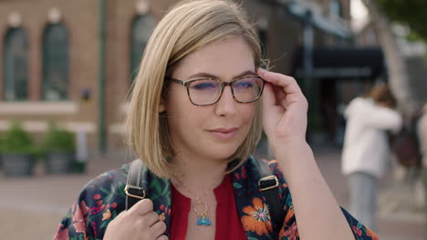 retrato de una hermosa mujer rubia de pie en la calle de la ciudad se pone gafas mirando a la cámara sonriendo con confianza