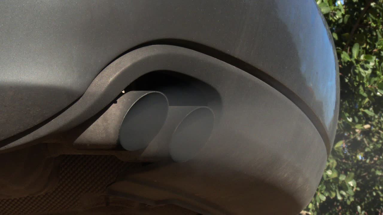 The twin tailpipe of a modern vehicle blowing out toxic emissions, close up