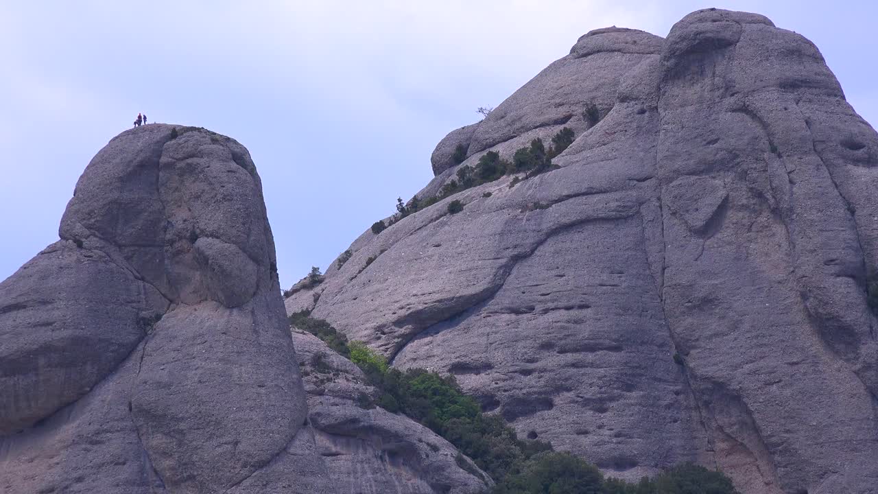 사람들은 스페인의 몬세라트 수도원 뒤에 있는 높은 산봉우리를 올라갑니다.