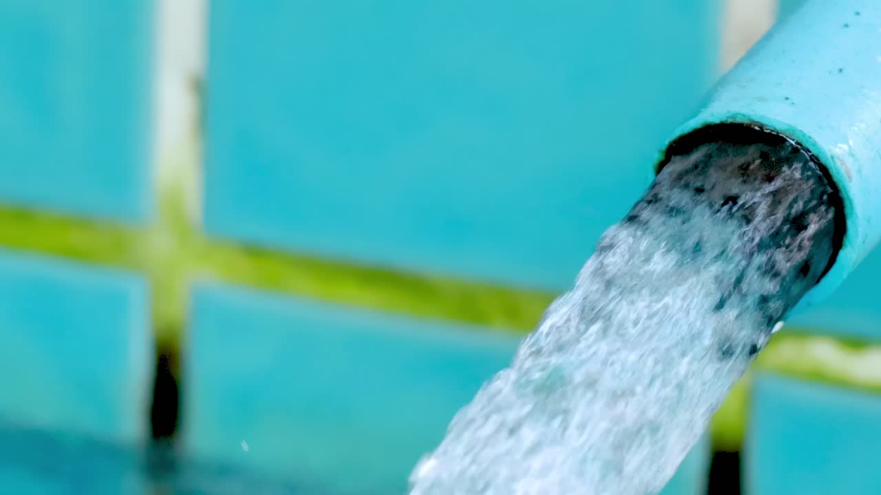 A steady stream of water flows from a blue pipe, set against a vibrant tiled background.