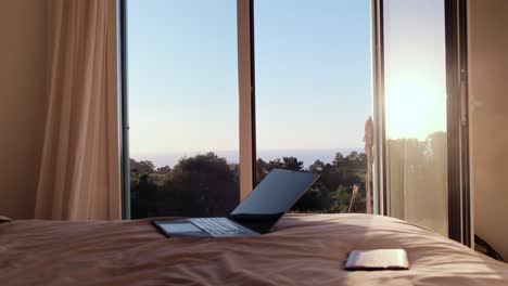 laptop on bed in a bright room with an open window and scenic view