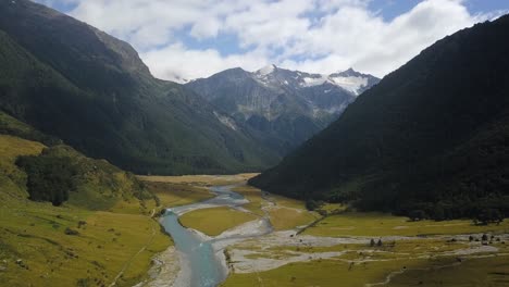 a forward aerial view over a river in a deep valley in new zealand heading towards snow peaked mountains