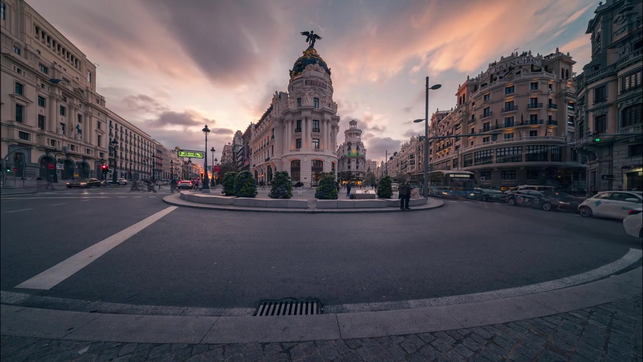 Časosběr od dne k noci ikonické budovy Metropolis v Madridu. Barevné západní oblohy přecházejí v městská světla, zatímco se doprava a chodci pohybují historickým centrem města.