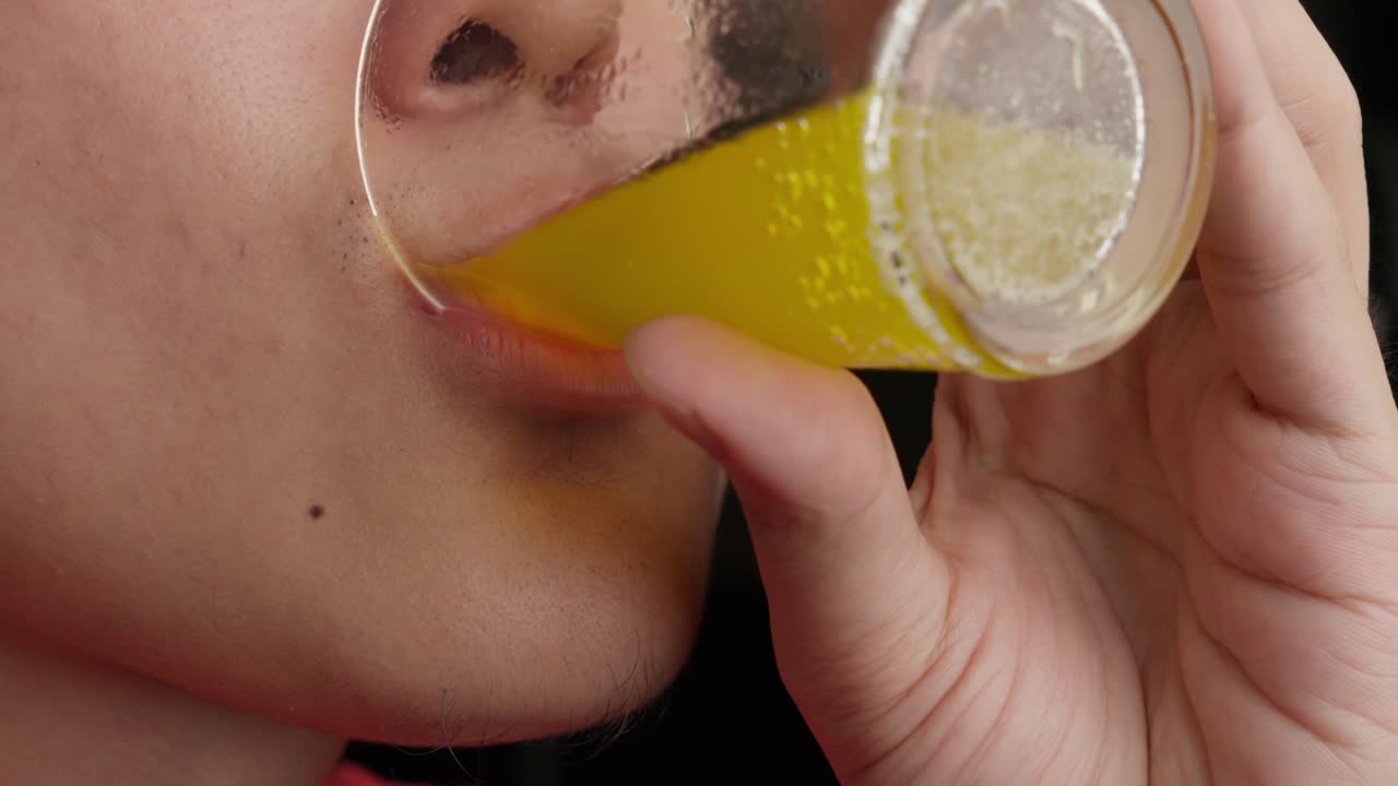 vista de cerca de la cara de un hombre bebiendo jugo amarillo de un vaso