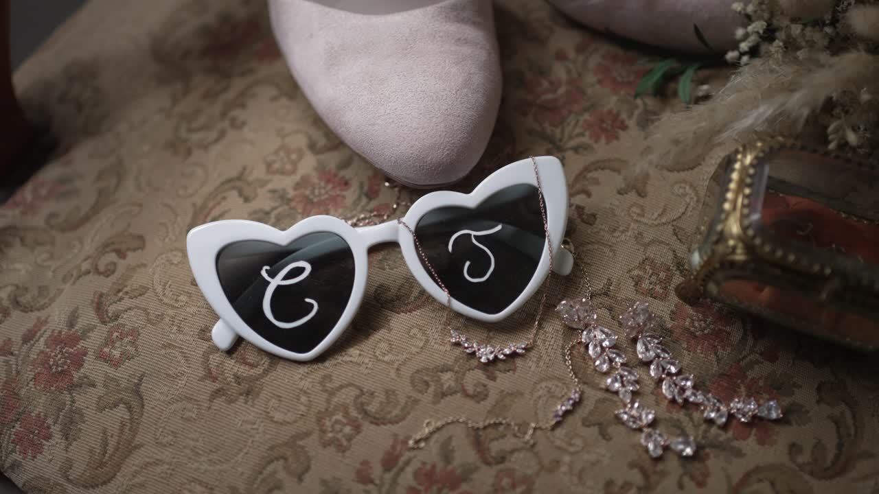 Flat lay of heart sunglasses jewelry shoes and bridal details on ornate patterned fabric