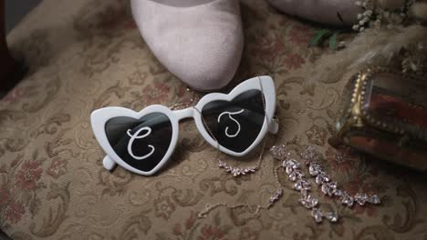 flat lay of heart sunglasses jewelry shoes and bridal details on ornate patterned fabric