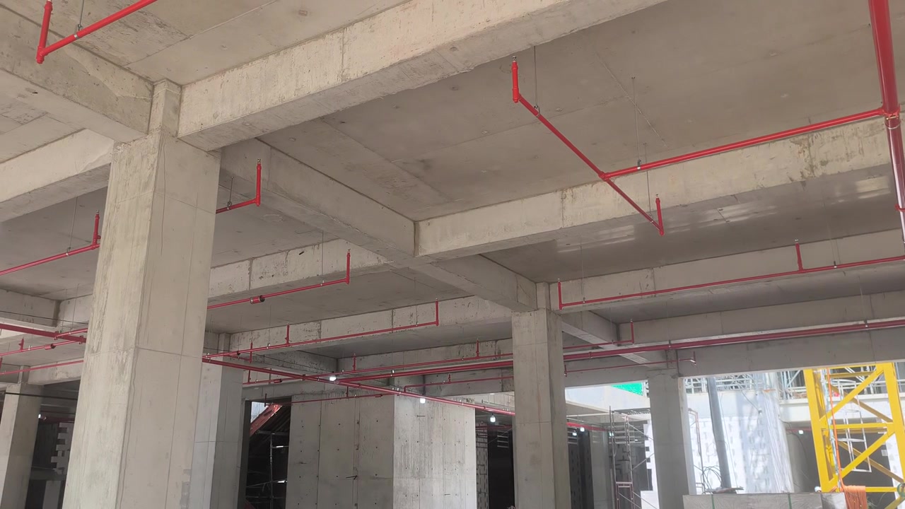 Operai installano una rete di tubazioni antincendio sprinkler in un cantiere edile. Realizzato secondo precisi progetti ingegneristici, questo sistema vitale eroga acqua per sopprimere gli incendi iniziali prima dell'arrivo dei vigili del fuoco