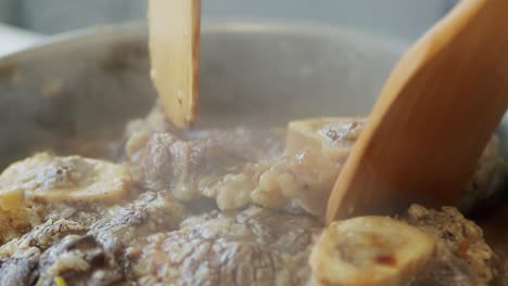 person stirring hot veal shanks in frying pan